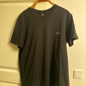 Svart BOSS t-shirt oanvänd - Svart t-shirt från BOSS med diskret logga på bröstet. Klassisk rund hals och korta ärmar. Tillverkad i mjuk bomull som känns skön mot huden. Enkel och stilren design som funkar till allt. Perfekt för dig som gillar minimalistisk stil. Pris kan diskuteras😊
