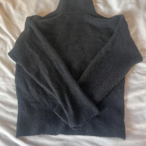 Svart stickad polotröja - Mysig svart stickad polotröja med lång ärm och hög krage. Perfekt för kyliga dagar och enkel att matcha med jeans eller kjol. Tröjan har en klassisk passform och är tillverkad i ett mjukt material som känns skönt mot huden.