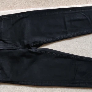 Svarta slim jeans från Uniqlo - Svarta jeans från Uniqlo i slim passform med raka ben och klassiska bakfickor. Materialet är en mix av bomull, polyester och elastan för skön stretch. Perfekt för dig som gillar stilrena och enkla jeans med snygg siluett.