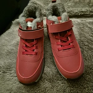 Röda sneakers med fuskpälsfoder - Snygga röda sneakers från Skotex med grått fuskpälsfoder för extra värme. Skorna har snörning, kardborreband och en rejäl svart sula med bra grepp. Perfekta för kyligare dagar och ger en sportig vibe till din outfit.
