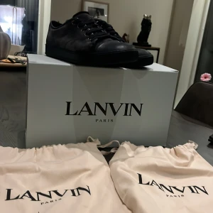 Mörk blå sneakers från Lanvin Paris - Snygga svarta sneakers från Lanvin Paris med rund tå och platt sula. Skorna har snörning med svarta skosnören och är tillverkade i skinn med en matt finish. Kommer med originalkartong och dustbags. Perfekt för dig som gillar stilrena och exklusiva sneakers.