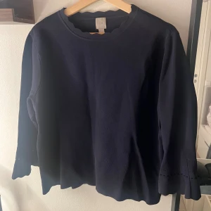 Mörkblå trekvartsärmad tröja H&M - Mörkblå trekvartsärmad tröja från H&M med vågiga kanter vid halsringning, ärmslut och nederkant. Tröjan är i mjukt material och har en enkel, stilren design som passar perfekt till jeans eller kjol.