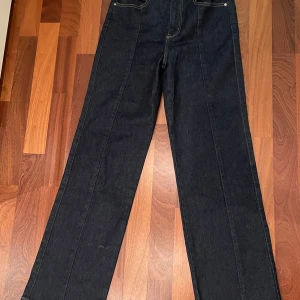 Mörkblå wide jeans från Gina Tricot - Säljer ett par mörkblå jeans från Gina Tricot, modell Perfect Jeans. De har en klassisk femficksdesign, hög midja och breda ben för en trendig siluett. Materialet är robust denim med snygga kontrastsömmar och silverfärgade detaljer. (ordinarie pris 500 kr)