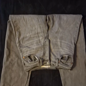 Grå Levi's Ribcage Straight Ankle jeans - Snygga grå Levi's Ribcage Straight Ankle jeans med klassisk femficksdesign och raka ben. Jeansen har hög midja och är tillverkade i slitstarkt denim med silverfärgade nitar och knapp. Perfekt för dig som gillar en clean och tidlös look.