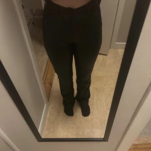 Svarta skinn byxor med hög midja - Snygga svarta byxor med rak passform och hög midja. Klassisk design med knapp och dragkedja framtill. Perfekta att styla med sneakers eller boots för en clean look. Materialet känns mjukt och följsamt mot kroppen.