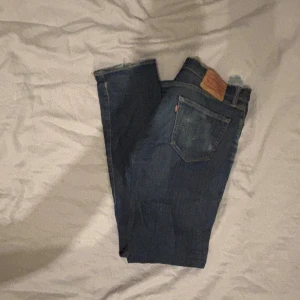 Levi's 511 mörkblå jeans - Snygga Levi's 511 jeans i mörkblå tvätt med klassisk femficksdesign och smal passform. Jeansen har en ikonisk läderpatch bak i midjan och subtila slitningar framtill. Perfekta för dig som gillar stilrena och tidlösa jeans.