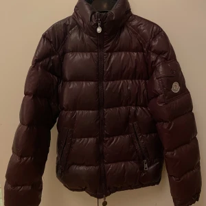 Mörkröd pufferjacka från Moncler - Säljer en snygg mörkröda pufferjacka från Moncler med hög krage och dragkedja framtill. Jackan har Moncler-logga på ärmen, två fickor med dragkedja och quiltad design. Perfekt för kalla dagar och riktigt skön att bära. Jag har tagit hand om den väldigt väl, då jag har älskat den otroligt mycket. Nu känner jag att det är dags för mig att köpa en ny och säljer den därför. Det är storlek 1 vilket jag skulle säga motsvarar S/XS