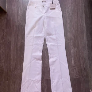 Vita bootcut-byxor från Chelsea XS - Snygga vita bootcut-byxor från Chelsea i storlek XS. Byxorna har klassisk knapp och dragkedja framtill, samt fickor på sidorna. Perfekt för dig som gillar stilrena och fräscha looks. Passar dig som vill ha en modern siluett.