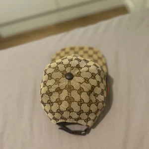 beige keps med gg monogram logga - Snygg beige keps från  klassiskt GG-monogram i brunt över hela kepsen. På sidan finns den ikoniska gröna och röda randen. Justerbar rem baktill i mörkbrunt. Perfekt för dig som vill ha en lyxig och trendig accessoar.