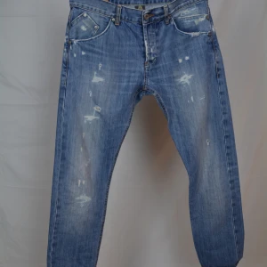 Dondup George - Feta blåa Dondup jeans i modellen George med slitningar. Jeansen är i storlek 32 och är i väldigt gott skick, dvs har inga tecken på användning. Innerbensmått: 69cm.    Midjemått: 41,5cm.     Vid frågor eller funderingar är det bara att höra av sig, och kom ihåg, alltid 14 dagars ångerrätt hos oss på Revalo!