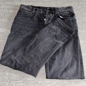 Svarta Nudie Jeans - Snygga svarta jeans från Nudie Jeans med klassisk femficksdesign och raka ben. Jeansen har knappgylf och bälteshällor, tillverkade i slitstarkt denim. Perfekta för dig som gillar en elegant stil. Hör av er vid intresse/ frågor!