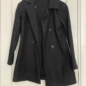Svart kappa från SHEIN, XS - Svart kappa från SHEIN i storlek XS med klassisk krage och dubbelknäppning framtill. Jackan har lång ärm och en rak, något utsvängd siluett. Materialet är mjukt och känns som ullblandning. Perfekt för dig som gillar stilrena och enkla plagg.