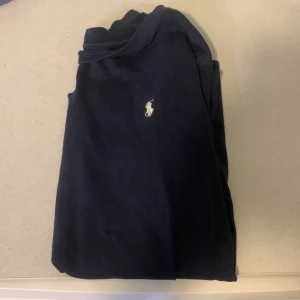 Marinblå t-shirt från Ralph Lauren - Snygg marinblå t-shirt från Ralph Lauren med klassisk vit logga broderad på bröstet. T-shirten har enkel design och är tillverkad i mjuk bomull som känns skön mot huden. Perfekt för dig som gillar stilrena plagg med ikonisk touch.