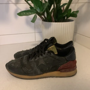 Valentino Rockrunner  - Snygga Valentino Rockrunner sneakers i svart med stjärnmönster och detaljer i mörkgrön och vinröd mocka. Skorna har snörning, platt sula och coola nitar med turkosa pärlor på hälen. Perfekt för dig som vill sticka ut med exklusiva och unika sneakers.