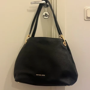 Svart axelväska från Michael Kors - I nytt skick!! Modellen raven, ordinariepris är  3945 kr. Dustbagen är lite smutsig. Köpt på Zalando! Orderbekräftelse kan visas upp om så önskas 🩷                                                                            Stilren svart axelväska från Michael Kors i mjukt skinn med guldfärgade metalldetaljer. Väskan har flera fack, inklusive ett med dragkedja, och rymlig insida med logomönstrat foder. Perfekt för dig som vill ha både funktion och snygg design.