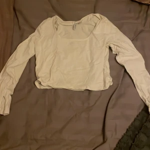 Vit långärmad topp från Boohoo - Säljer en enkel och stilren vit långärmad topp från Boohoo. Toppen har en fyrkantig urringning framtill och är croppad i modellen. Materialet känns mjukt och lätt, perfekt för att matcha med jeans eller kjol. Passformen är normal och toppen är ärmlös baktill.