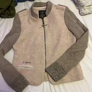 Beige stickad jacka från L'Argentina - Snygg beige jacka från L'Argentina med stickade grå ärmar och muddar. Jackan har dragkedja framtill, diskret broderad logga och coola detaljer vid axlarna. 