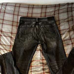 Svarta straight jeans från jack and Jones - Säljer ett par svarta jeans från Levi's med klassisk femficksdesign och raka ben. Jeansen har en snygg tvättad look och normal passform. Perfekt för dig som gillar stilrena och tidlösa jeans med cool vibe.