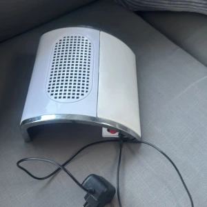 Elektrisk dammsugare för nageldamm - Effektiv elektrisk dammsugare för nageldamm med dubbla fläktar. Perfekt för manikyr och salongsbruk. Utrustad med strömbrytare och nätadapter. Vit design med kromdetaljer, i gott skick med mindre ytslitage. Fångar effektivt damm vid nagelbehandling.