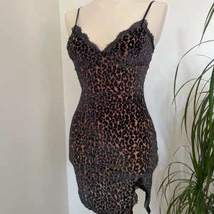 Leopardmönstrad kort klänning med spets - Säljer en snygg leopardmönstrad kort klänning med tunna axelband och spetsdetaljer vid halsringningen och nederkanten. Klänningen har en tight passform och är perfekt för dig som vill sticka ut med ett djuriskt mönster och coola detaljer.