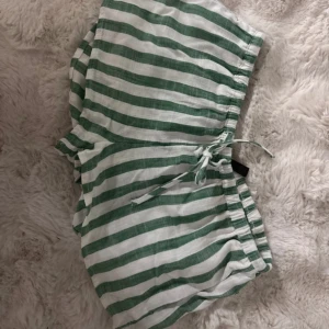 Randiga gröna och vita shorts med snörning - Säljer ett par chill randiga shorts i grönt och vitt med skön snörning i midjan. De är gjorda i ett lätt och luftigt material, perfekta för varma dagar. Passformen är loose och de har en avslappnad vibe.