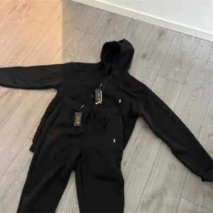 Svarta mjukisbyxor och hoodie  från Polo Ralph Lauren - Svarta mjukisbyxor från Polo Ralph Lauren med klassisk logga broderad på benet. Byxorna har snörning i midjan och är gjorda i mjukt bomullsmaterial för maximal komfort. Perfekt för chill dagar eller när du vill vara extra bekväm . 