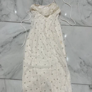 Oh polly pärlprydd kortklänning - Säljer den billigt då den behöver kemtvättas. Superfin vit kortklänning med massor av pärlor och små glaspärlor över hela tyget. Klänningen har smala axelband och en elegant, lite lös passform. Perfekt för dig som vill sticka ut med en unik och glittrig look. Materialet känns lyxigt och detaljerna är verkligen iögonfallande.