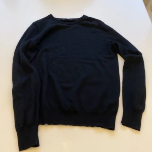 Svart stickad tröja från Uniqlo - En stilren svart stickad tröja från Uniqlo i storlek M. Tröjan har rund hals och långa ärmar med ribbade muddar vid ärmslut och nederkant. Perfekt för dig som gillar enkel och klassisk design med skön passform.