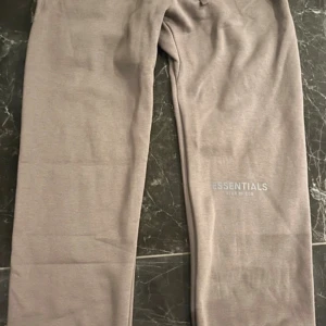 Grå Essentials mjukisbyxor Fear of God - Snygga grå mjukisbyxor från Essentials Fear of God med logga på benet och bakficka. Byxorna har elastisk midja och är tillverkade i mjukt bomullsmaterial. Perfekta för en chill och avslappnad stil. Kom gärna med prisförslag.