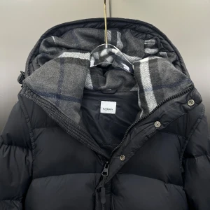 Burberry jacka/väst - Svart pufferjacka från Burberry med avtagbara ärmar, huva med snörning och stor logopatch på ena ärmen. Jackan har dragkedja och knappar framtill samt quiltad design. Fodret är i rutigt mönster i grått och blått. Perfekt för kalla dagar och riktigt snygg streetstil. Helt ny aldrig använd