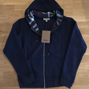 Burberry hoodie  - Detta är en marinblå Burberry London-hoodie med hel dragkedja och dragsko i huvan. Den är i utmärkt skick med etiketter på.  ⭐️ Skick: 10/10 🎲 Storlek: L 🎨 Färg: Marinblå 📦 Snabb och trygg frakt. 