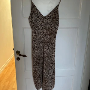 Leopardmönstrad långklänning från H&M - Säljer en långklänning från H&M med leopardmönster i beige och svart. Klänningen har smala axelband, v-ringning och är figurnära med ett snyggt fall. Perfekt för dig som vill sticka ut med ett djurmönster och en trendig siluett.
