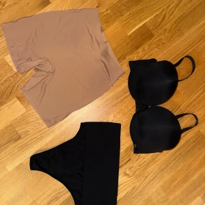 Svart bandeau tubtopp - Säljer en svart bandeau tubtopp med bred resår upptill för extra stöd. Toppen är ärmlös och har en clean, enkel design som är perfekt att styla med olika outfits. Materialet känns mjukt och stretchigt mot huden. Underdelar med shapewear i nytt skick. Strl M, 75C