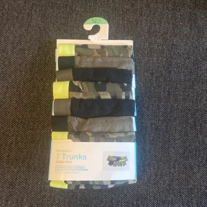 7-pack camo och svarta trunks  - Säljer ett 7-pack trunks i storlek 146 cm för kids 10-11 år. Mixen innehåller camouflagemönstrade och svarta shorts med coola detaljer i neon-gult. Materialet är bomullsrikt för skön känsla hela dagen.