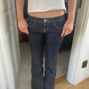 Mörkblå bootcut lågmidjade jeans - Snygga mörkblå jeans med bootcut och låg midja. Jeansen har kontrasterande vita sömmar och klassisk femficksdesign. Passformen är normal och materialet är robust denim som sitter skönt. De är i storlek S/36. Säljer då de inte kommer till användning ❤️