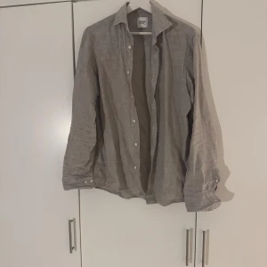 Linneskjorta från Oscar of Sweden - Snygg grå skjorta från Oscar of Sweden i slim fit och mjukt linne. Skjortan har klassisk krage, långa ärmar med manschett och vita knappar framtill. Perfekt för dig som gillar en chill och stilren look. Passar dig som vill ha något luftigt och bekvämt.