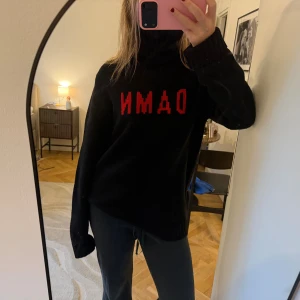 Svart polotröja Zadig  - Svart polotröja med lång ärm och röd DAMN-text framtill. Tröjan är stickad och har en hög krage som går att vika ner eller ha uppe. Passformen är lite oversize, jag är 169, står ej storlek men tror M/L, köpt för några år sen i Paris 