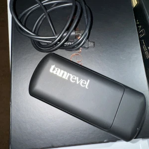 Tanrevel Spray Tan Device - Tanrevel portabel spray tan-enhet i svart, med original USB-laddkabel och förpackning. Enheten ser ut att vara i gott skick utan synliga repor eller skador. Perfekt för smidig och jämn brun-utan-sol applicering hemma eller på resan.