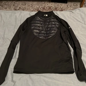 Svart Nike Therma-Fit tröja XL - Nike Therma-Fit tröja i svart med quiltad, glansig panel framtill och half zip-dragkedja. Långärmad. XL i barn storlek 