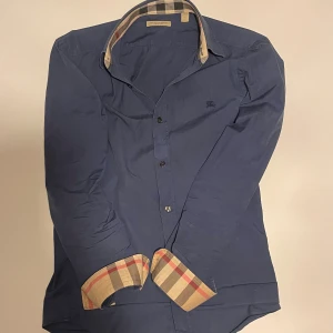 Blå Burberry skjorta - Säljer nu denna snygga Burberry skjortan till ett bra pris. Skjortan säljs då den börjar bli för liten och hänger just nu i garderoben. Den är självklart äkta och köpt på NK för cirka 5000kr. Ställ om det skulle finnas några frågor! 