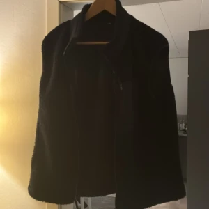 Svart fleeceväst med dragkedja - Mysig svart fleeceväst med hög krage och hel dragkedja framtill. Västen har en praktisk bröstficka med dragkedja och två sidofickor. Perfekt att slänga på över en hoodie för extra värme. Enkel, stilren och riktigt skön.