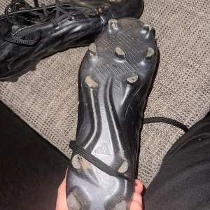 Svarta adidas fotbollsskor med dobbar - Säljer ett par helsvarta adidas fotbollsskor med klassisk design och snörning. Skorna har rund tå, platt sula med fasta dobbar och är tillverkade i syntetmaterial. Perfekta för dig som vill ha en clean look på planen. Pris kan diskuteras 