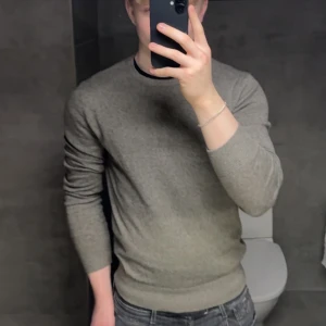 Grå stickad tröja Tiger of Sweden - grå/grön stickad tröja från Tiger of Sweden med rund hals och ribbade muddar vid ärmslut och nederkant. Slim passform och passar till jeans eller chinos. Enkel och stilren design som funkar året runt. Använd en gång och säljer pga att den är för kort. Tunn i materialet. Köpt på NK för 1299 kr. Sitter som visat på 180 cm, 80 kg.