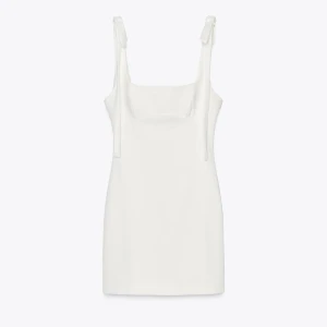 Vit kortklänning med knytband - Supersnygg vit kortklänning med raka linjer och knytband på axlarna. Klänningen har en stilren och minimalistisk design med fyrkantig urringning och ärmlös modell. Perfekt för dig som gillar enkel men chic stil.