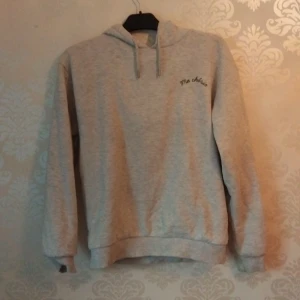 Grå hoodie Ma chérie Gina Tricot - Ljusgrå hoodie från Gina Tricot med svart text 'Ma chérie' framtill och ett större tryck med hjärta och pil på ryggen. Tröjan har huva med snörning och är tillverkad i mjuk bomullsblandning. Perfekt för en chill och avslappnad stil.