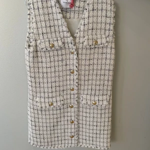 Rutig väst från Anine Bing i bomull - Stilren rutig väst från Anine Bing i vit och svart bomullsblandning. Västen har guldknappar framtill, två bröstfickor med lock och råa kanter för en trendig look. Perfekt att styla över en skjorta eller t-shirt.