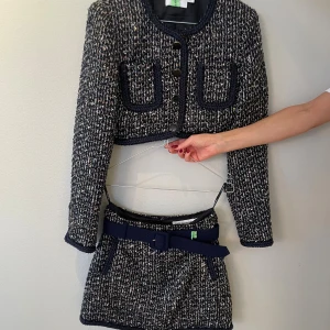 Mörkblå tweedkjol med bälte - Snygg kort kjol i mörkblå tweed med inslag av vitt och diskreta färgdetaljer. Kjolen har ett matchande mörkblått bälte i midjan och en klassisk, rak passform. Perfekt för dig som gillar en chic och trendig look.