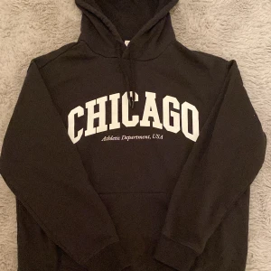 Svart hoodie Chicago H&M M - Svart hoodie från H&M i storlek M med stor vit CHICAGO-print och texten 'Athletic Department, USA' på bröstet. Tröjan har huva med snörning och en klassisk magficka. Hoodien är inte särskilt tjock utan tunn. Passar både kvinnor och män. Använd ett fåtal gånger. 