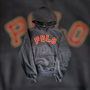 Svart hoodie från Polo Ralph Lauren - Snygg svart hoodie från Polo Ralph Lauren med stor röd POLO-text broderad på bröstet. Klassisk känguruficka framtill och justerbar huva. Perfekt för en avslappnad och trendig streetwear-look.