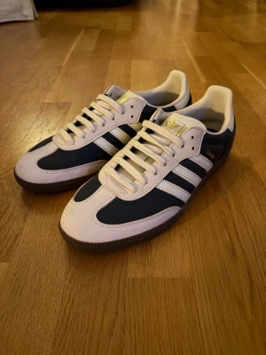 Adidas Samba sneakers marinblå/vita - Säljer ett par unika och riktigt feta Sambas i marinblått och vitt som jag fick i julklapp. Skorna har de ikoniska tre ränderna på sidan, gulddetaljer på plösen och snörning framtill. Går för över 2000 kronor på andra plattformar. Säljer då dem inte riktigt passade. BVSA